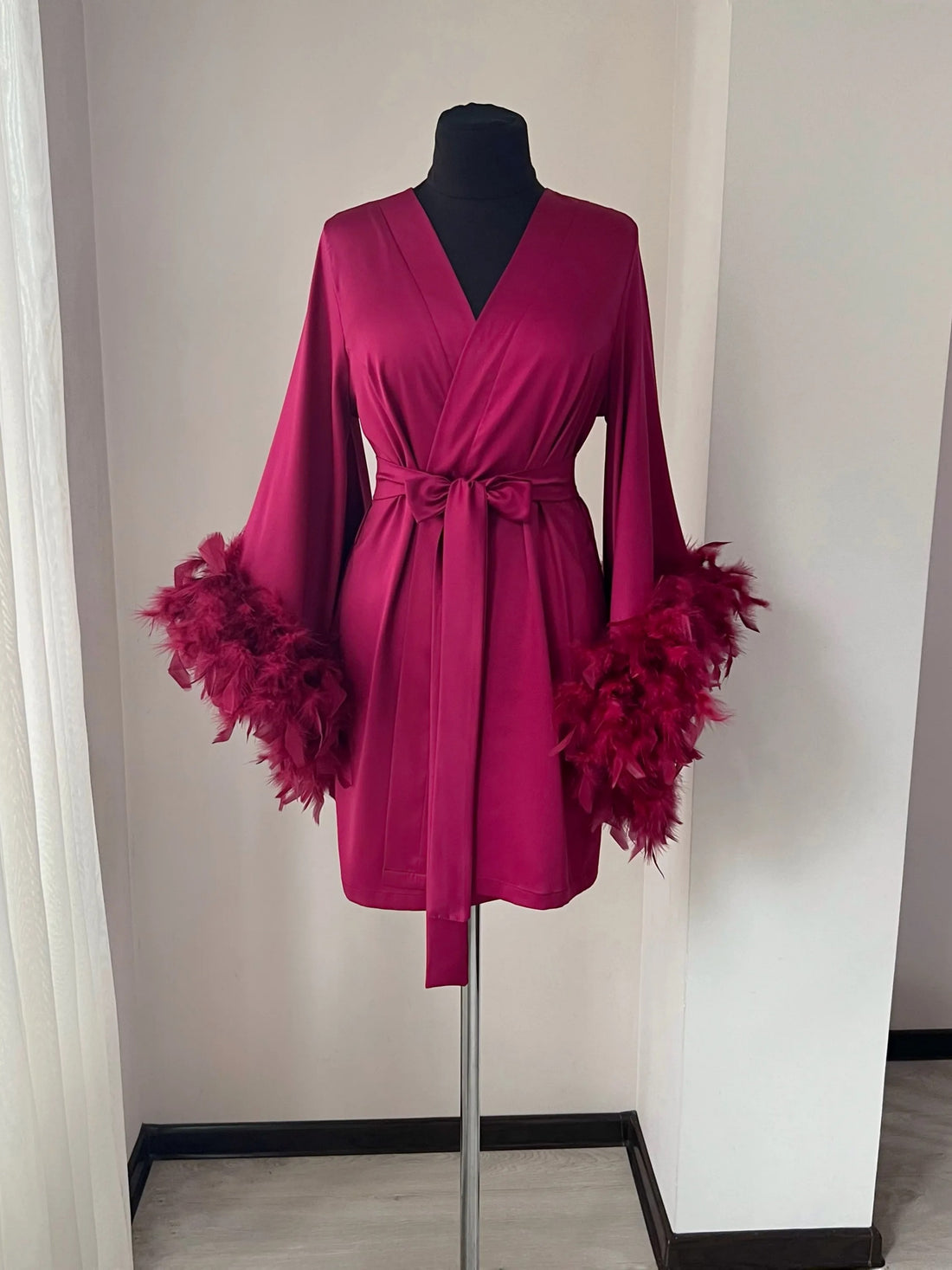 A mannequin wearing a vibrant pink robe with long sleeves and feather accents, displayed on a mannequin stand.