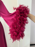 A close-up view of a person's arm wearing a vibrant pink feathered garment, with the feathers appearing to be made of a shiny material.
