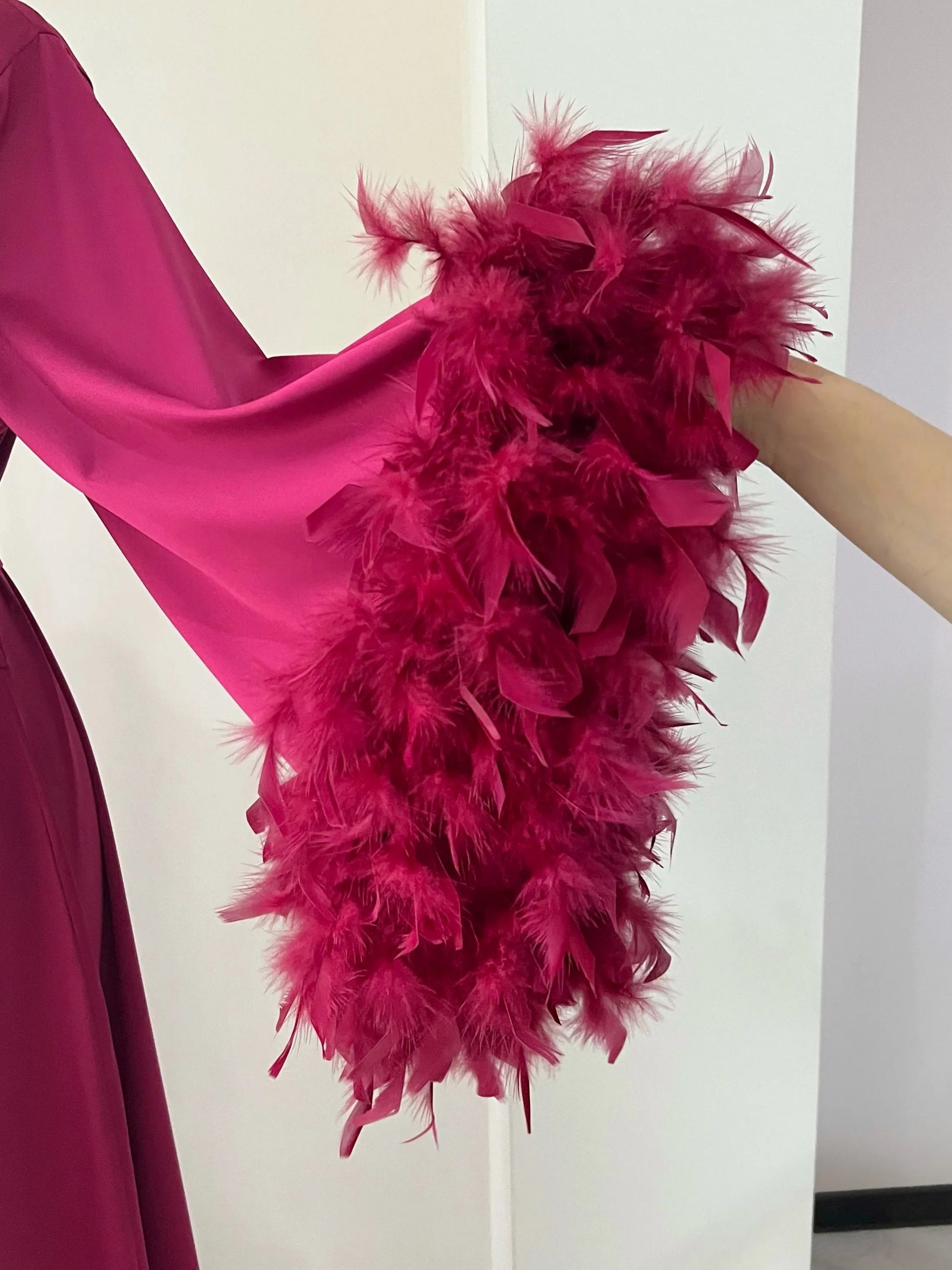 A close-up view of a person's arm wearing a vibrant pink feathered garment, with the feathers appearing to be made of a shiny material.
