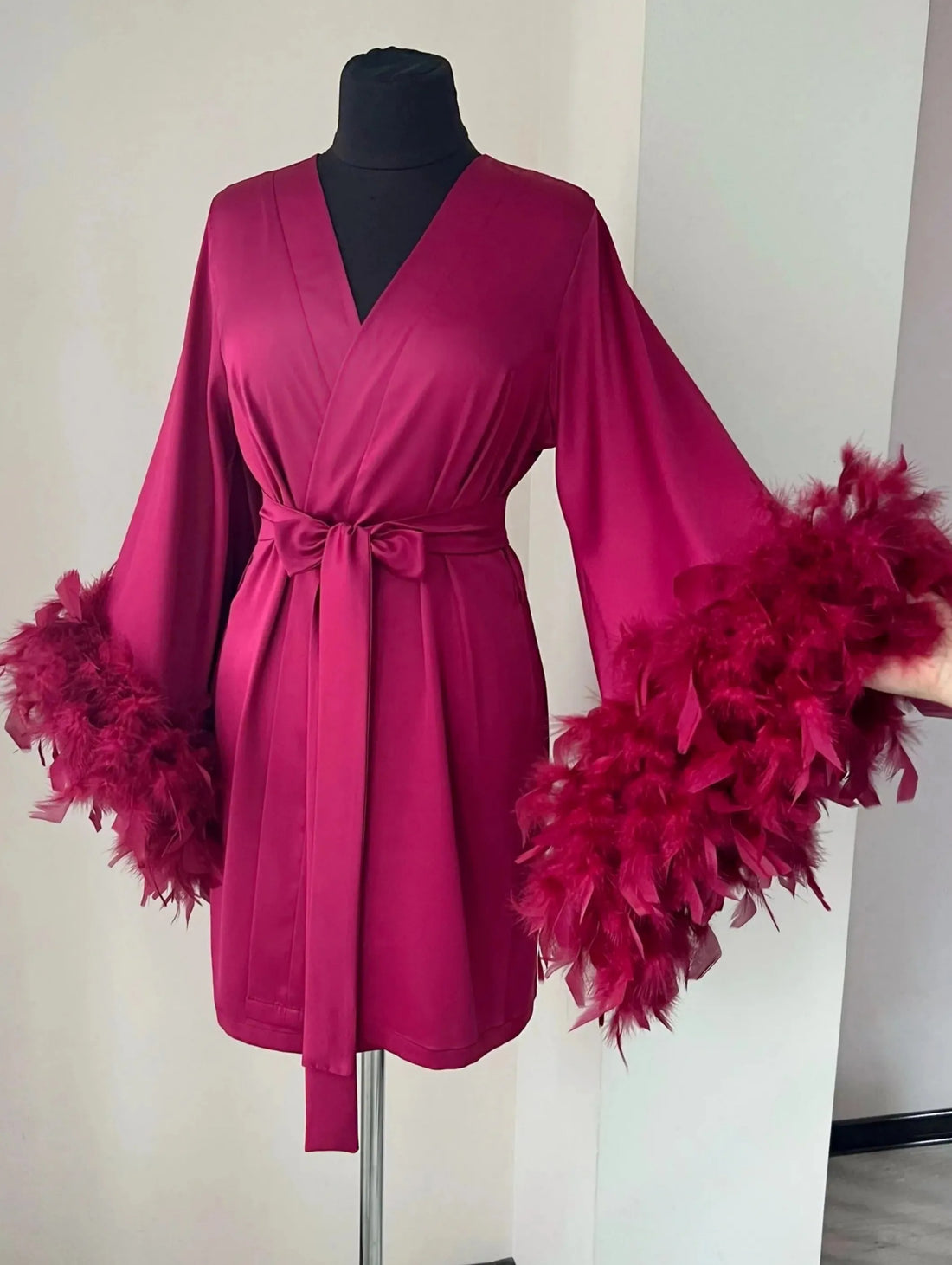 A mannequin wearing a vibrant pink robe with long sleeves and feather accents, displayed on a mannequin stand.