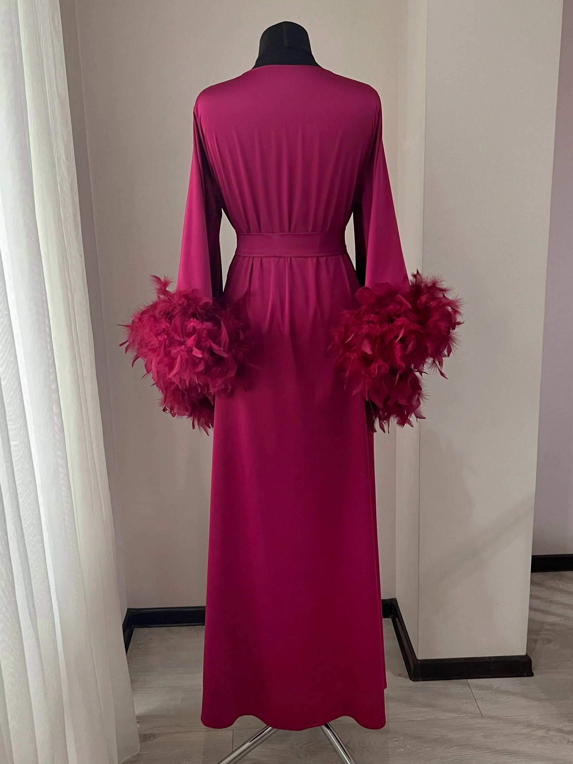 A long, burgundy-colored robe with feather accents, displayed on a mannequin.