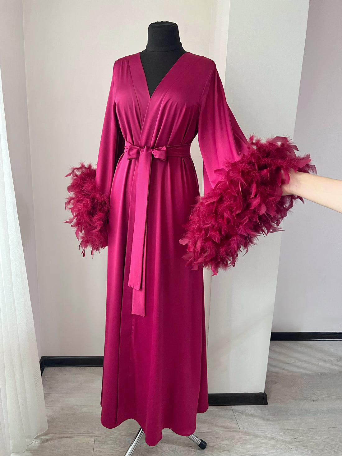 A mannequin wearing a long, pink satin robe with feather accents.