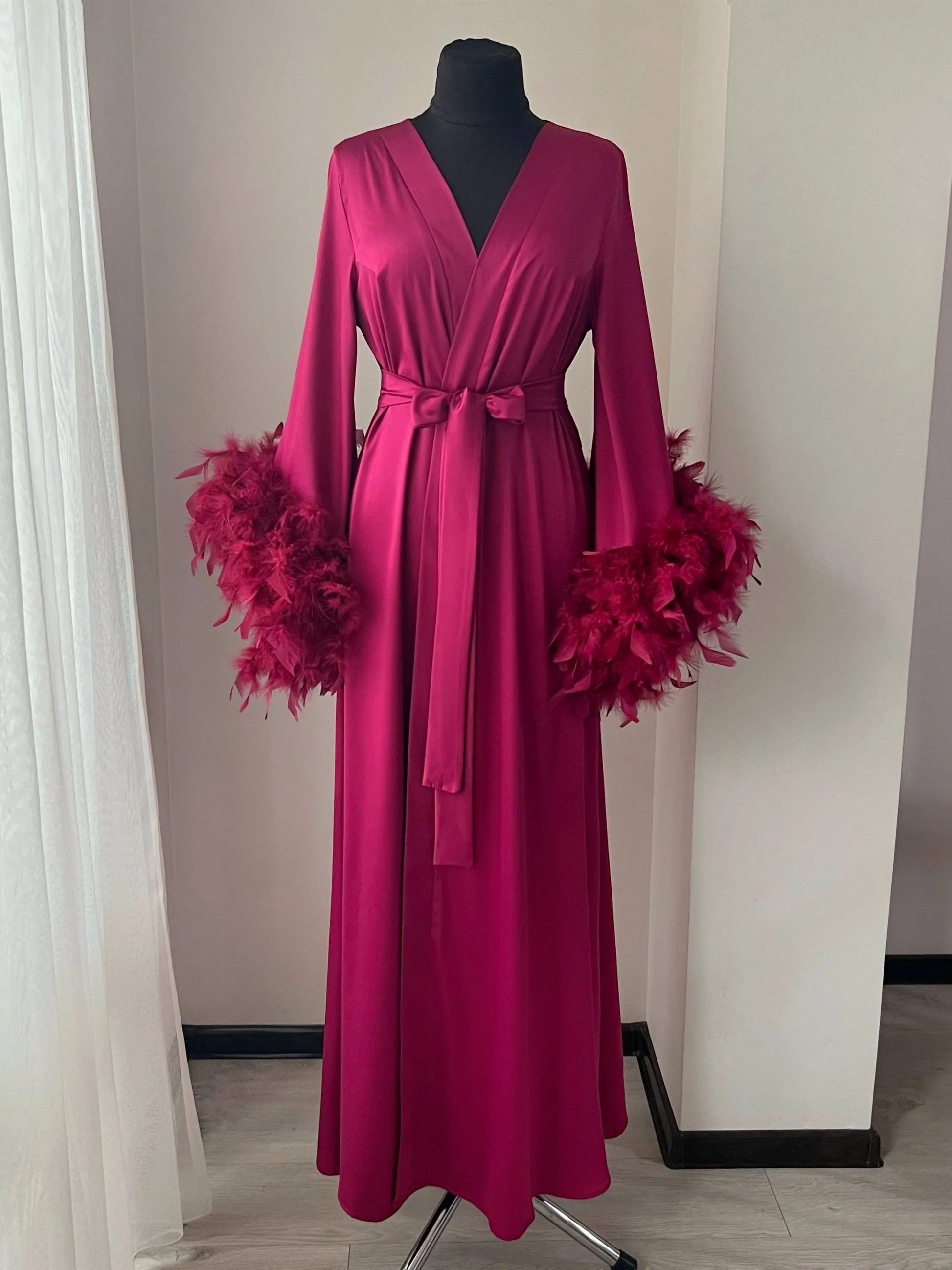 A long, pink robe with feather accents displayed on a mannequin.