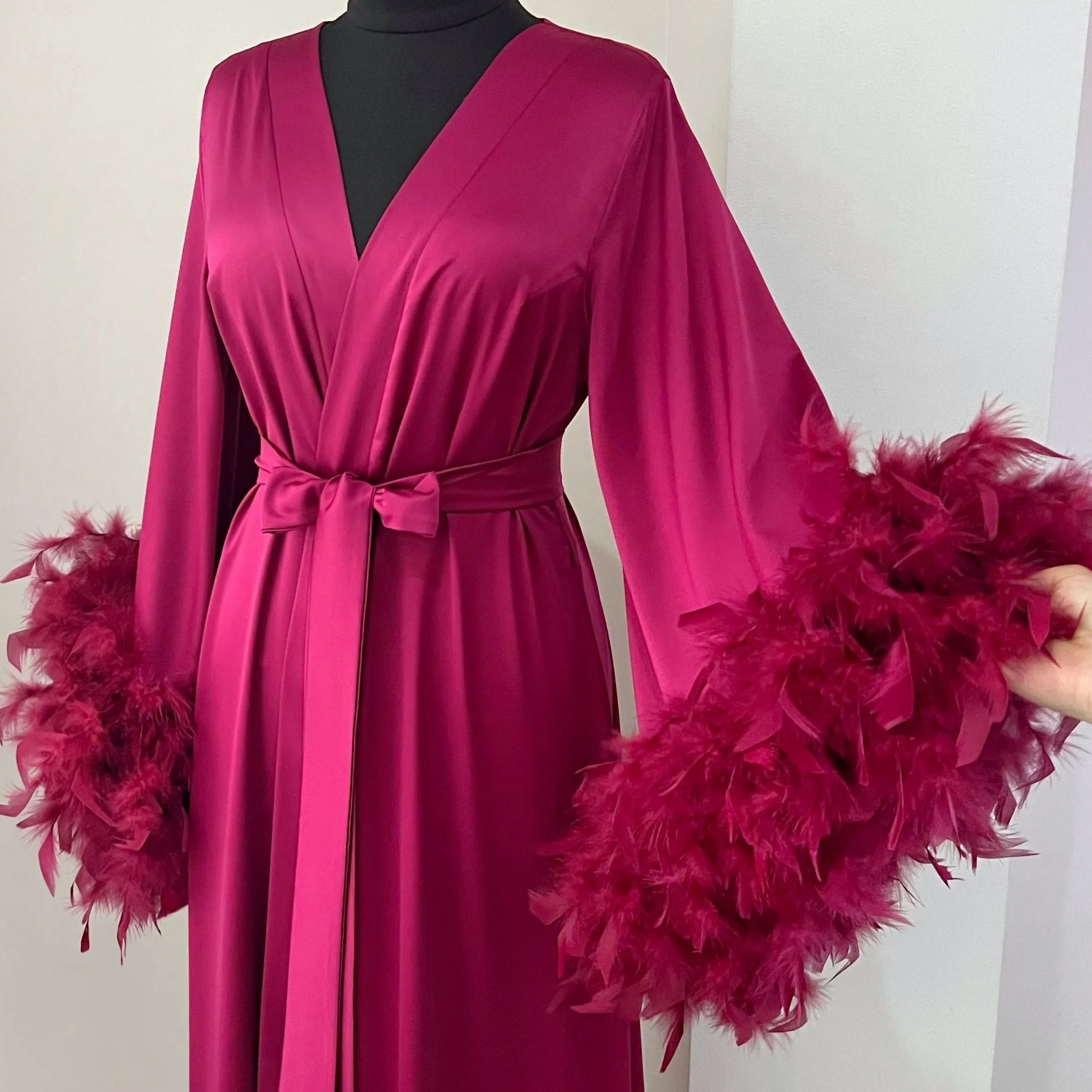A mannequin wearing a long, pink satin robe with feather accents.