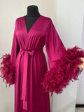 A mannequin wearing a long, pink satin robe with feather accents.