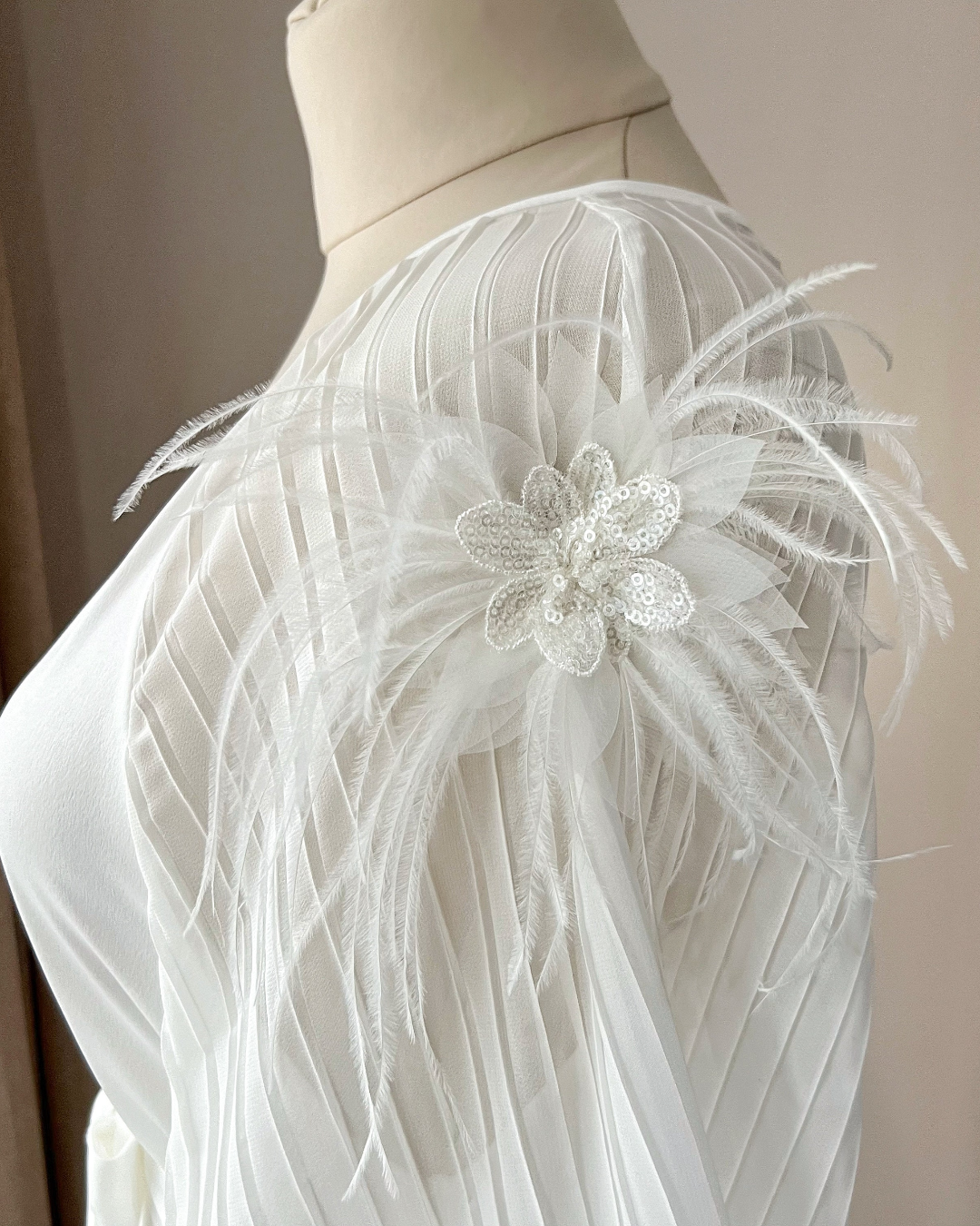 a white dress with a flower and feathers on it