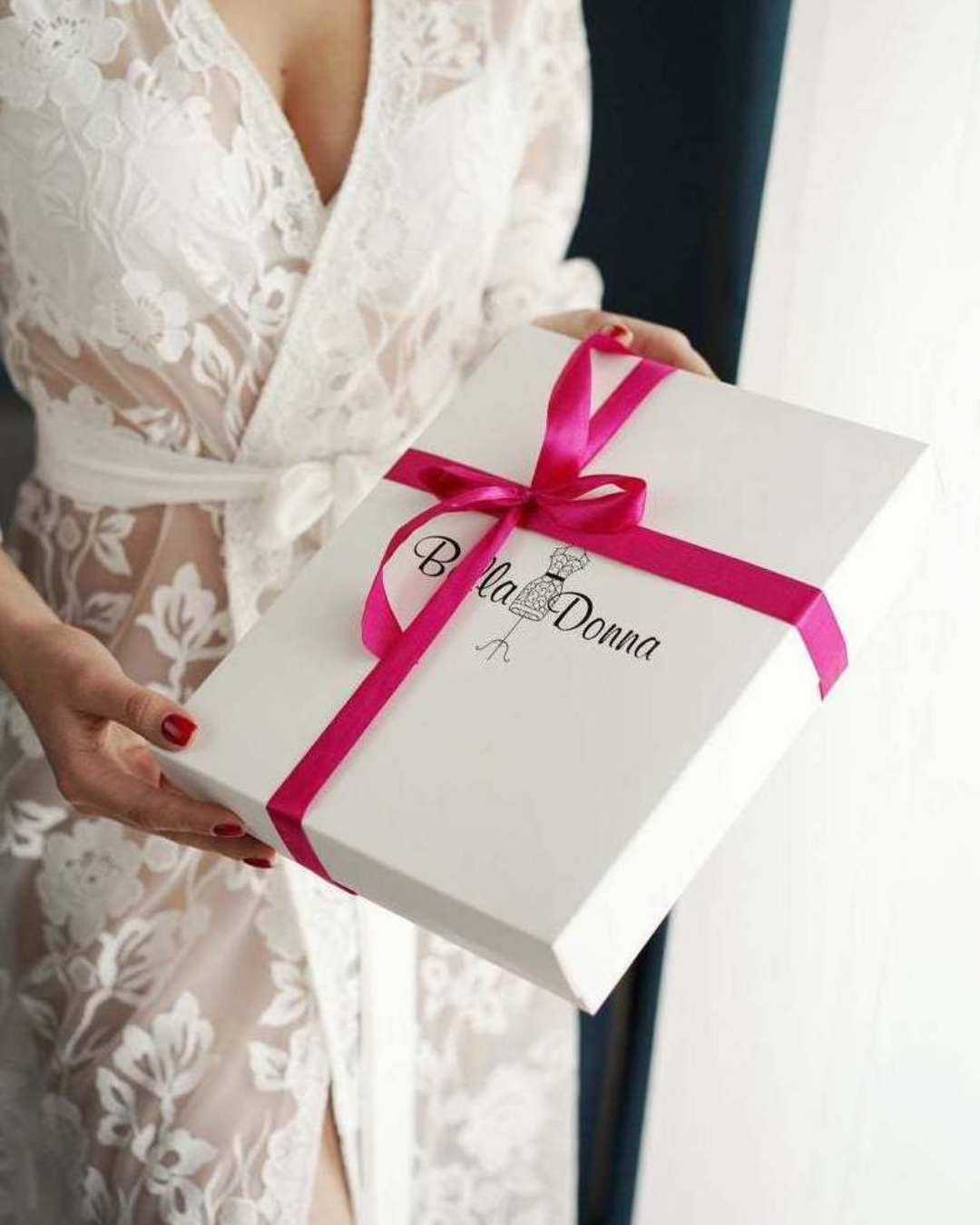 a woman holding a white box with a pink ribbon